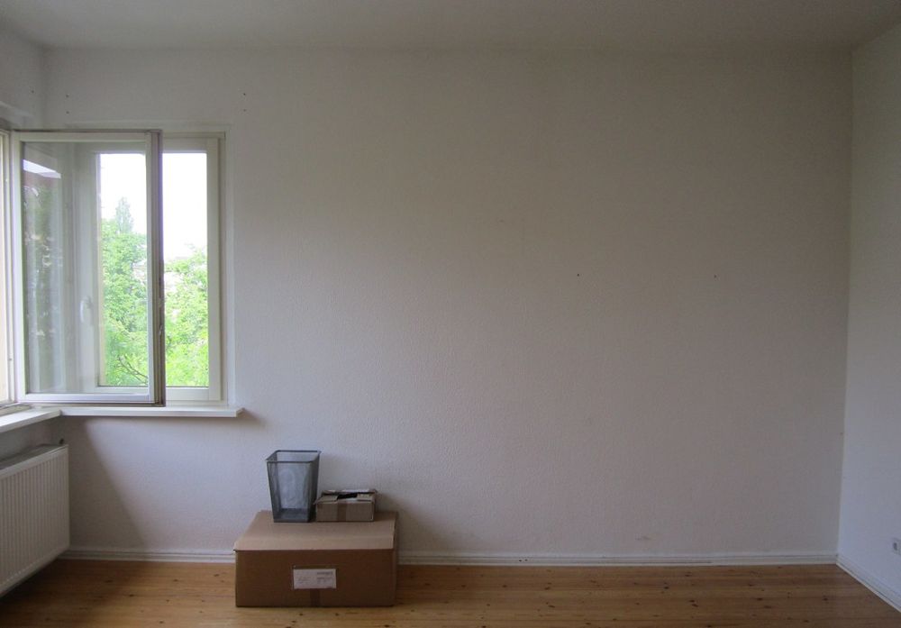An empty white room with one window, a cardboard box and a wastepaper basket
