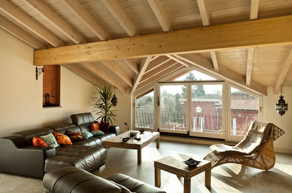 A sunlit attic loft with exposed wooden beams, huge windows and a leather sofa that has seen things