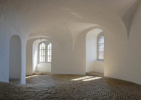 A round white room with vaulted ceilings, arched windows and a spiral cobblestone floor
